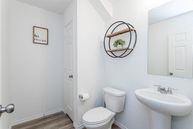 half bath featuring a sink, baseboards, toilet, and wood finished floors