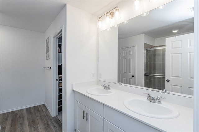 full bath with double vanity, tiled shower, wood finished floors, and a sink