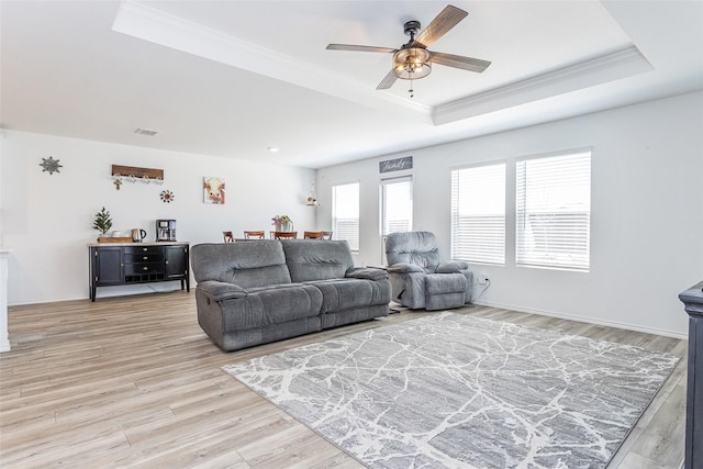 living area with ceiling fan, a tray ceiling, light wood-style flooring, and ornamental molding