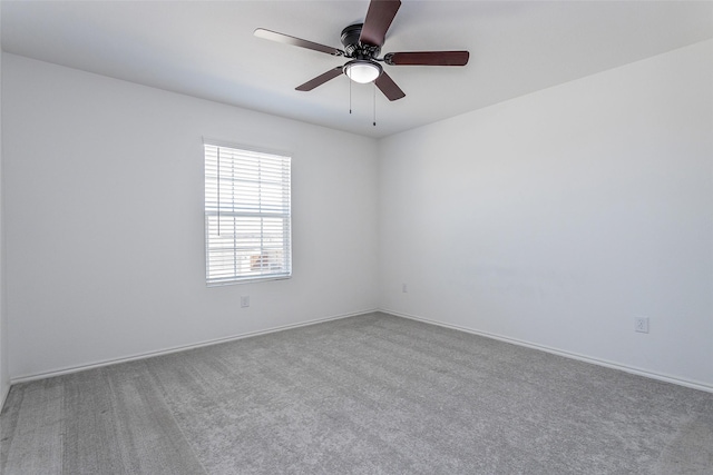 carpeted spare room featuring baseboards and a ceiling fan