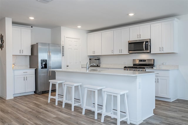 kitchen featuring a center island with sink, a breakfast bar area, stainless steel appliances, and light wood-style floors