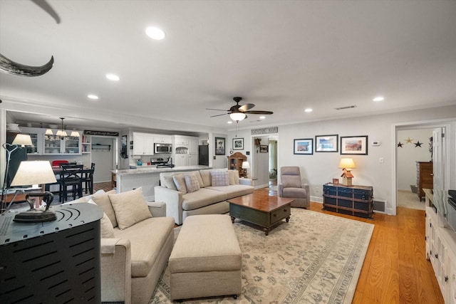 living room with visible vents, baseboards, recessed lighting, light wood-style floors, and ceiling fan with notable chandelier