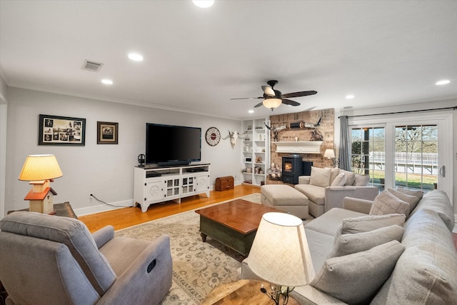 living area featuring visible vents, a ceiling fan, wood finished floors, crown molding, and a brick fireplace