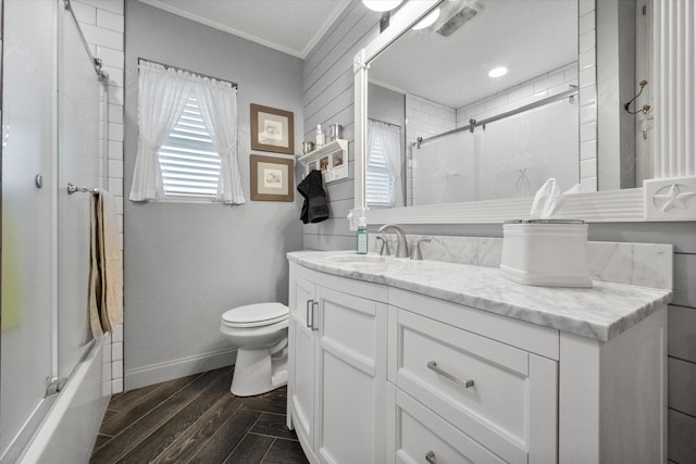 full bath with vanity, wood finished floors, baseboards, toilet, and combined bath / shower with glass door