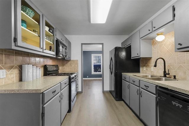 kitchen with light wood finished floors, gray cabinets, black appliances, and a sink