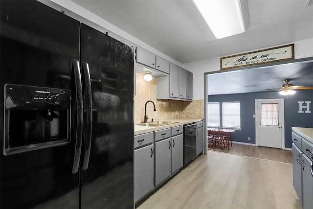 kitchen with tasteful backsplash, gray cabinetry, light wood-style floors, black appliances, and a sink