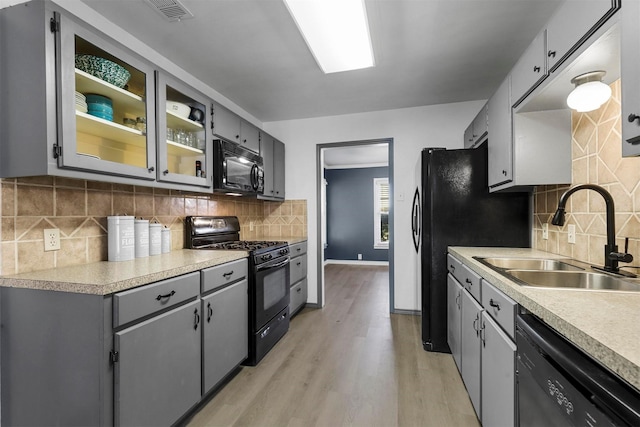 kitchen featuring gray cabinets, black appliances, light wood-type flooring, and a sink