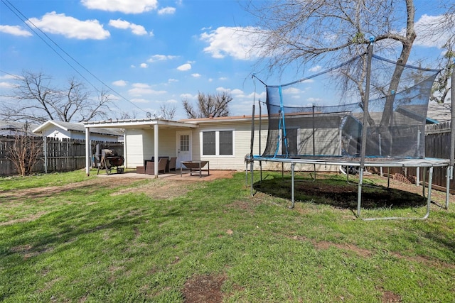 rear view of house with a yard, a trampoline, a fenced backyard, and a patio area