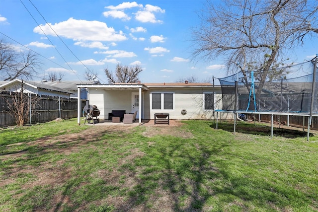 back of house with a patio area, a trampoline, a lawn, and fence