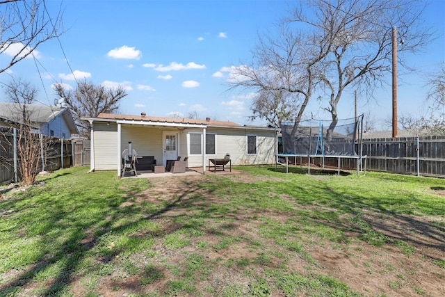 rear view of property with a patio area, a trampoline, a fenced backyard, and a yard