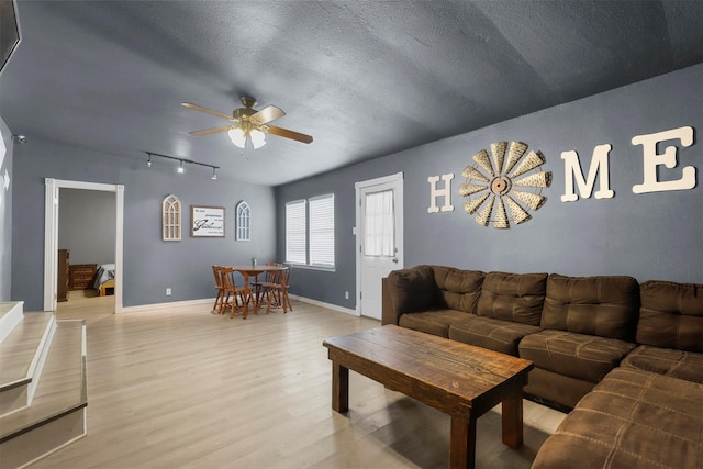 living area featuring baseboards, ceiling fan, light wood-type flooring, rail lighting, and a textured ceiling