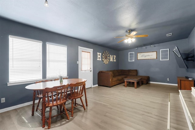 dining area featuring a textured ceiling, light wood-style floors, rail lighting, baseboards, and ceiling fan