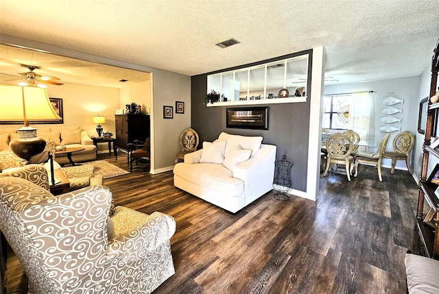 living room featuring visible vents, a textured ceiling, wood finished floors, baseboards, and ceiling fan