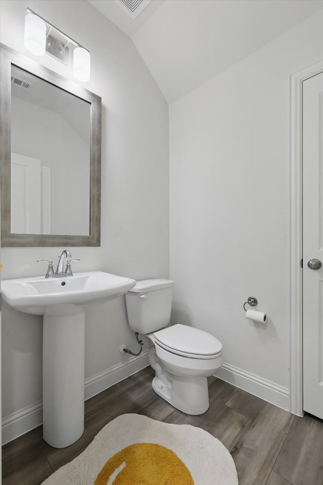 half bath with visible vents, baseboards, toilet, lofted ceiling, and wood finished floors