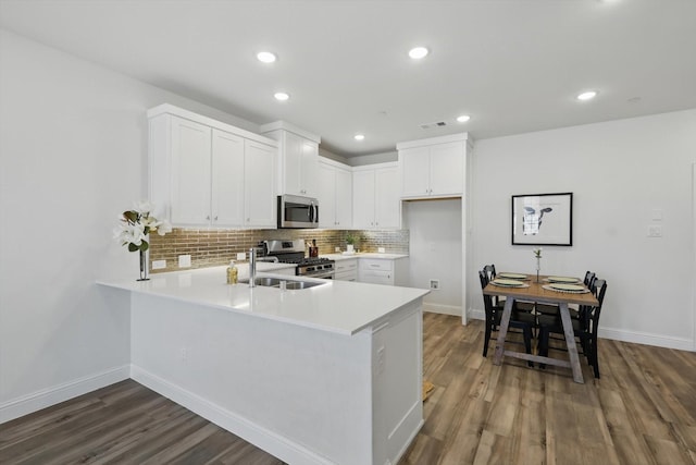 kitchen with tasteful backsplash, light countertops, appliances with stainless steel finishes, a peninsula, and a sink