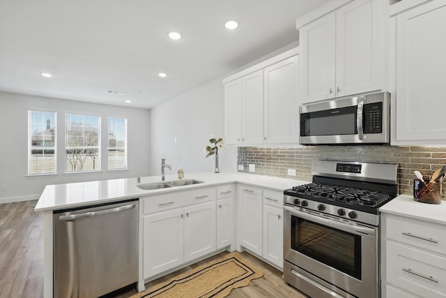 kitchen with backsplash, light countertops, a peninsula, stainless steel appliances, and a sink