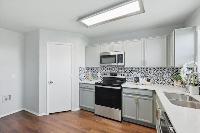 kitchen with tasteful backsplash, light countertops, gray cabinets, dark wood-style floors, and stainless steel appliances