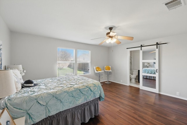 bedroom featuring visible vents, baseboards, a barn door, and wood finished floors