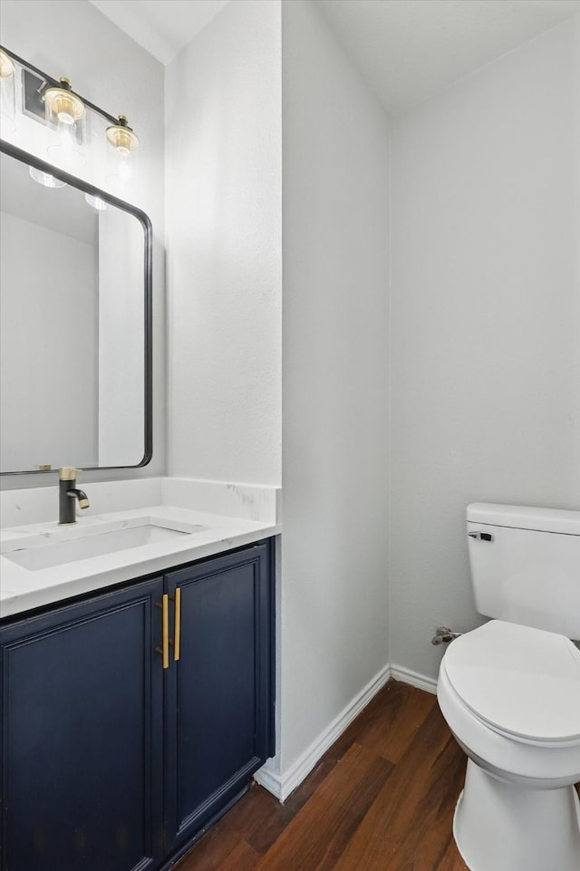 half bath featuring toilet, vanity, baseboards, and wood finished floors