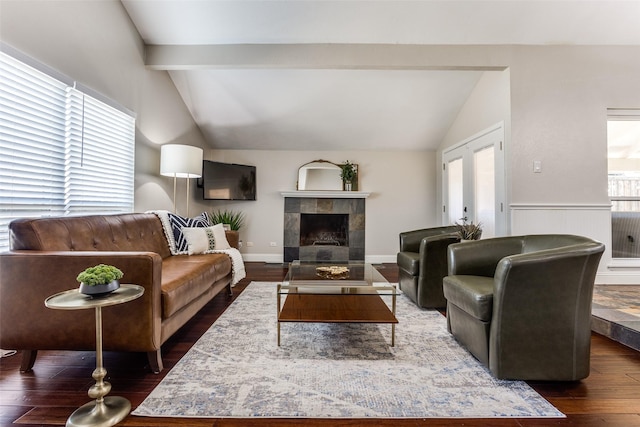 living room featuring dark wood-style floors, a tile fireplace, vaulted ceiling with beams, and baseboards