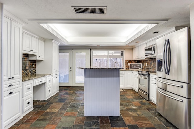 kitchen featuring a tray ceiling, visible vents, appliances with stainless steel finishes, and stone finish floor