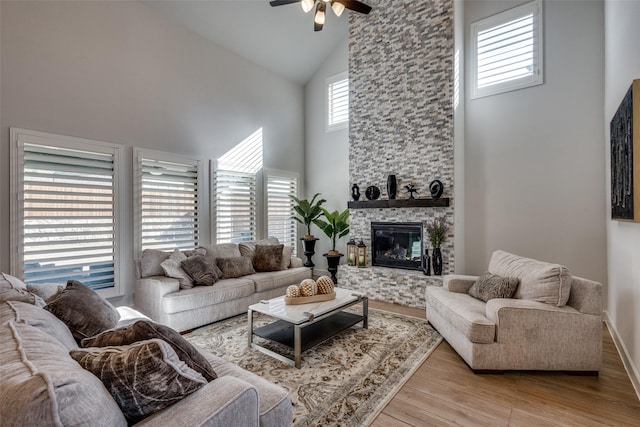 living area with light wood finished floors, a fireplace, high vaulted ceiling, and a ceiling fan