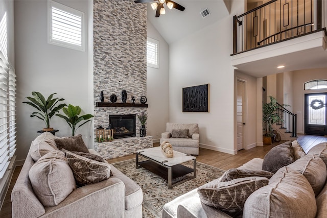 living area featuring visible vents, a ceiling fan, wood finished floors, a stone fireplace, and stairs