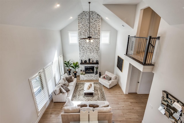 living room featuring a fireplace, a ceiling fan, light wood finished floors, and high vaulted ceiling