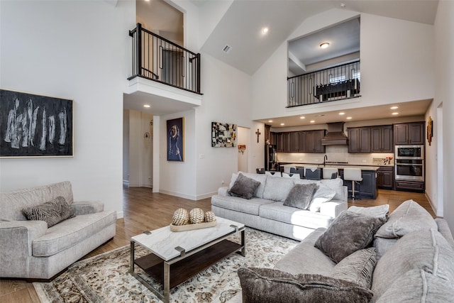 living room featuring recessed lighting, baseboards, light wood finished floors, and high vaulted ceiling