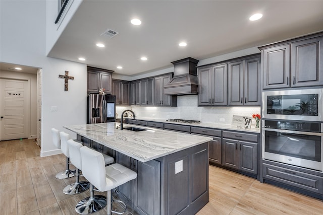 kitchen with premium range hood, a sink, light stone counters, tasteful backsplash, and appliances with stainless steel finishes