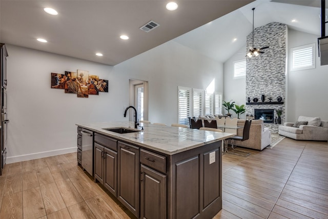 kitchen with visible vents, a sink, a stone fireplace, dark brown cabinets, and light wood-style floors