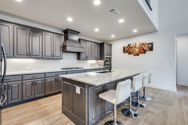 kitchen with a breakfast bar area, visible vents, stainless steel gas cooktop, custom exhaust hood, and a sink