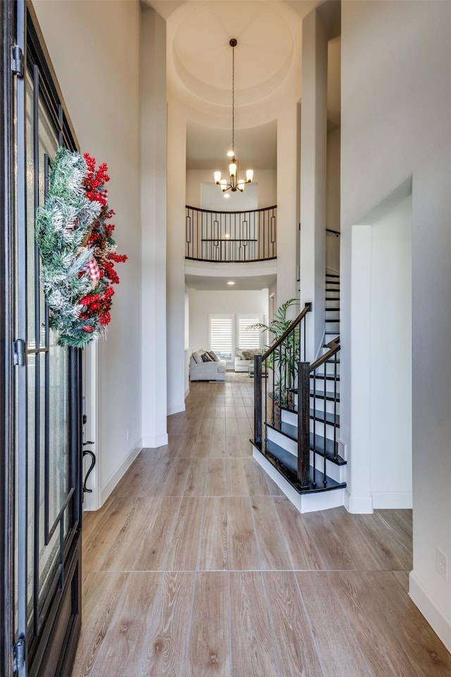 entryway featuring baseboards, stairs, a high ceiling, wood finished floors, and a notable chandelier