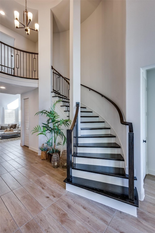 stairway with a chandelier, baseboards, a towering ceiling, and wood finished floors