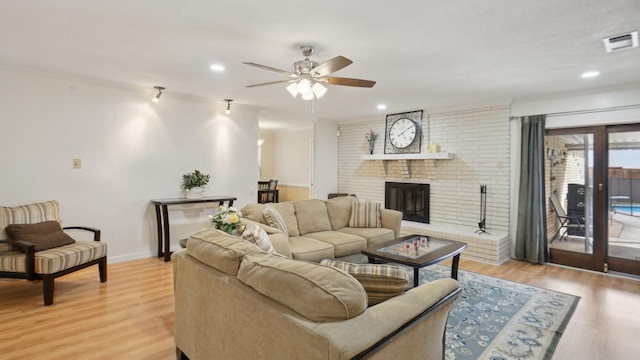 living area with a brick fireplace, light wood-style floors, visible vents, and ceiling fan