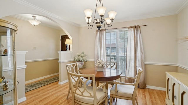 dining room featuring arched walkways, crown molding, light wood-style floors, and an inviting chandelier