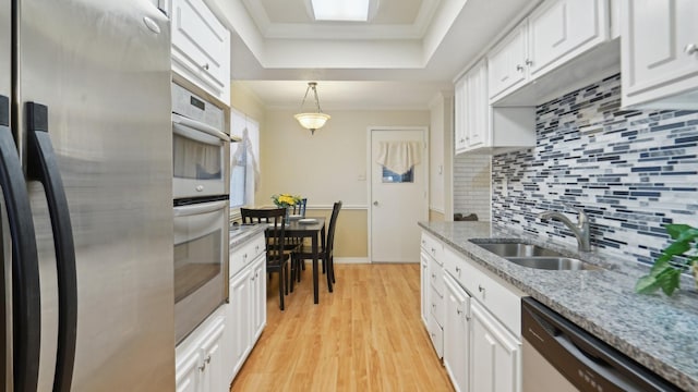 kitchen featuring a sink, a tray ceiling, white cabinetry, stainless steel appliances, and crown molding