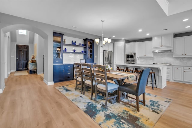 dining space with baseboards, recessed lighting, light wood-style flooring, an inviting chandelier, and arched walkways