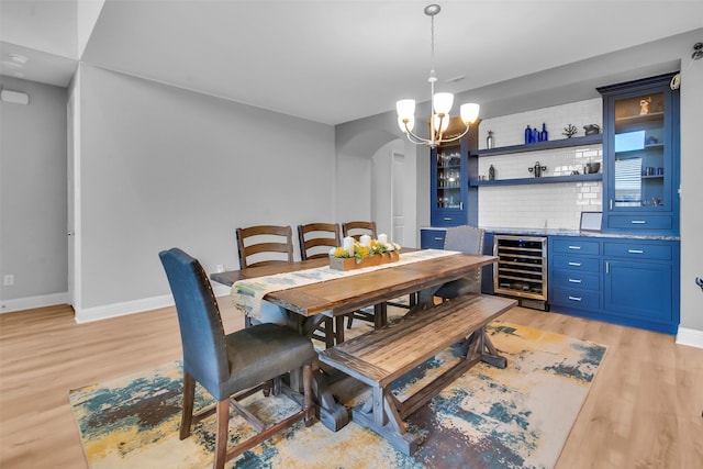 dining area featuring indoor wet bar, a notable chandelier, light wood-type flooring, and baseboards