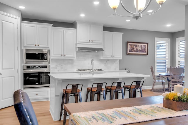 kitchen with light wood finished floors, under cabinet range hood, light countertops, appliances with stainless steel finishes, and white cabinetry