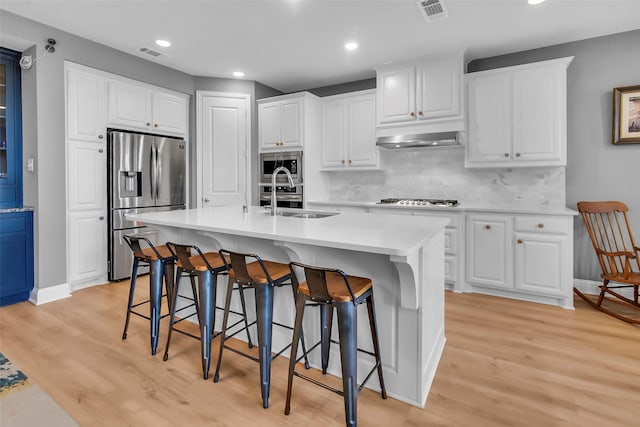 kitchen featuring visible vents, light wood-type flooring, a sink, a kitchen breakfast bar, and appliances with stainless steel finishes