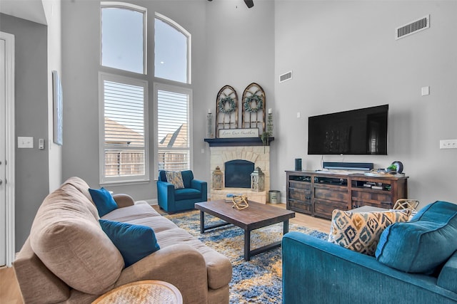 living room with visible vents, a fireplace, a towering ceiling, and wood finished floors