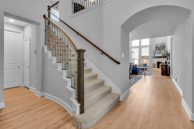 stairway featuring baseboards, arched walkways, wood finished floors, and a towering ceiling