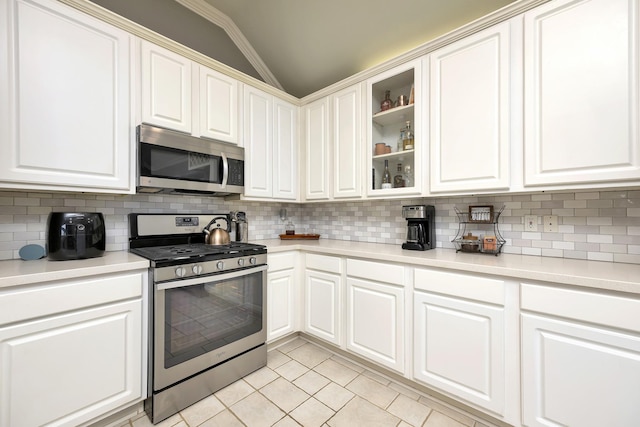 kitchen featuring appliances with stainless steel finishes, light tile patterned floors, lofted ceiling, tasteful backsplash, and glass insert cabinets