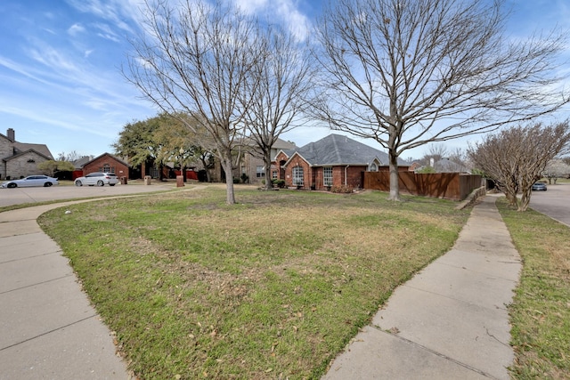 view of front facade featuring brick siding, fence, and a front yard