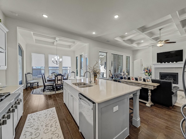 kitchen with a sink, dark wood-type flooring, ceiling fan with notable chandelier, coffered ceiling, and stainless steel dishwasher