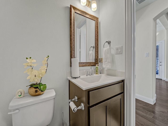 half bath featuring vanity, toilet, wood finished floors, and baseboards