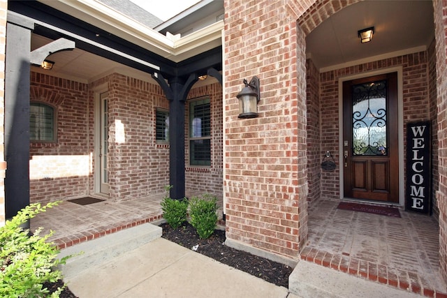 doorway to property featuring a porch and brick siding