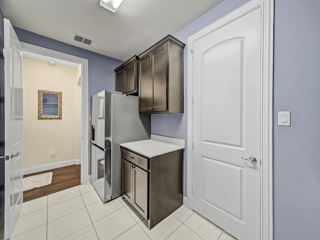 kitchen featuring visible vents, dark brown cabinetry, stainless steel fridge with ice dispenser, light countertops, and light tile patterned floors