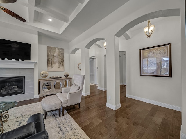 living area featuring beamed ceiling, coffered ceiling, wood finished floors, arched walkways, and baseboards